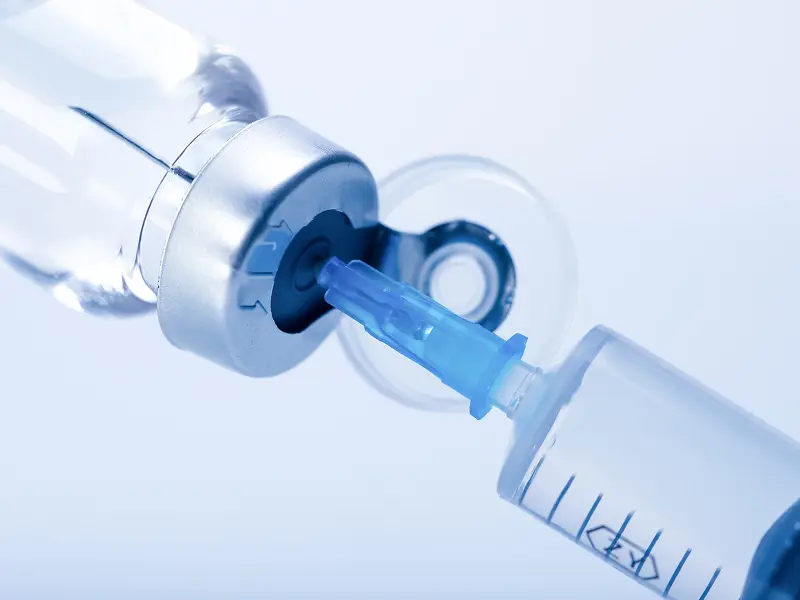 Sterile syringe drawing lyophilized solution from a laboratory glass vial during reconstitution protocols.